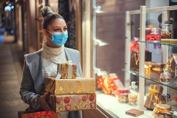  woman wearing mask holding wrapped holiday gifts