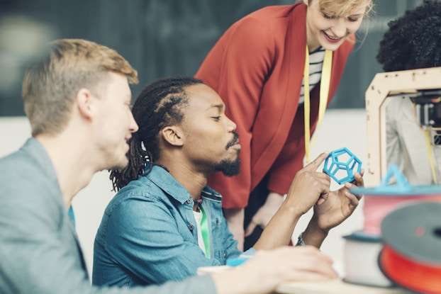  Team of people looking at an object created by a 3D printer.