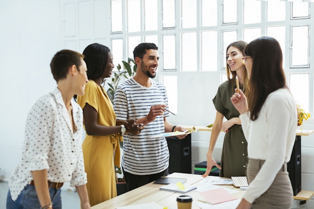 Group of coworkers standing around a table in a group discussing work.