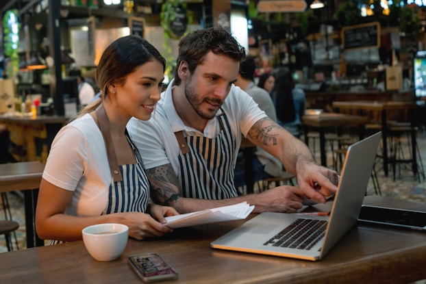 Two co-workers working on a laptop in their cafe.