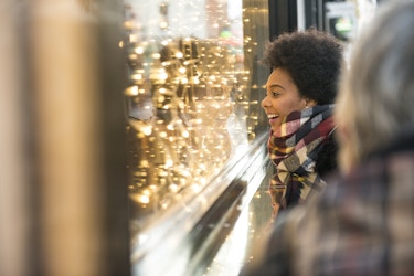  Smiling woman looking into a retailer's window with holiday lights displayed. 