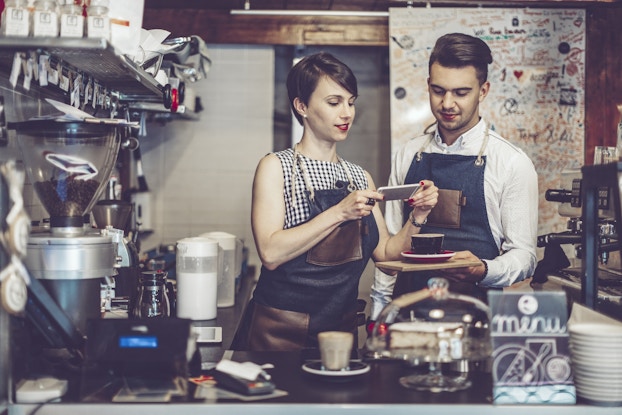 Baristas take a photo of latte art to promote cafe on social media.