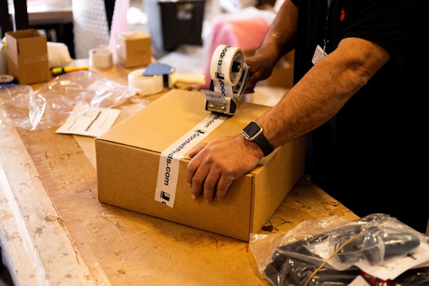 Person's hands sealing a GoodwillFinds box with packing tape.