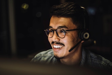  A smiling male customer service representatives uses a headset to talk to a customer via a call center service. 