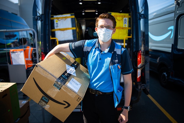 Amazon delivery driver wearing a mask and holding an Amazon package.