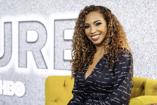 A waist-up shot of Grow With Google digital coach Angelina Darrisaw. She sits on a yellow couch against a wall made to look like TV static. The HBO logo is positioned near the bottom of the wall, underneath part of a larger word (the letters "TURE").