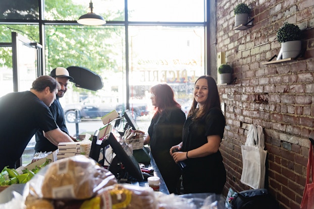  Zero-waste shop owner smiles as her employee checks out customers in her sunlit shop