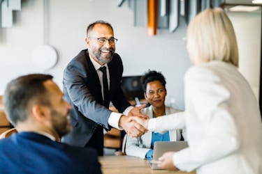 Two business professionals are shown. They are standing and shaking hands. The handshake signals a successful negotiation of a business-to-business sales transaction.