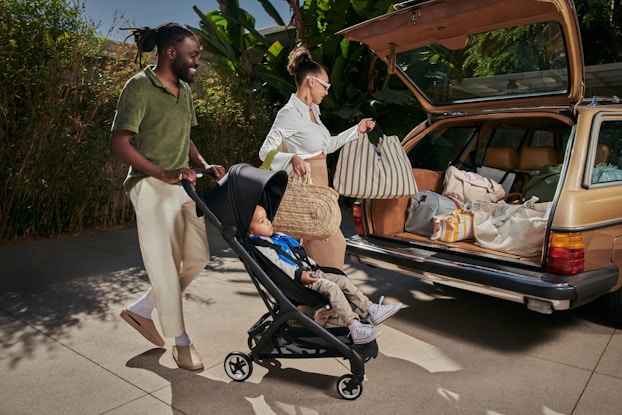  Two parents loading the trunk of their car while their child sits in a Bugaboo stroller.