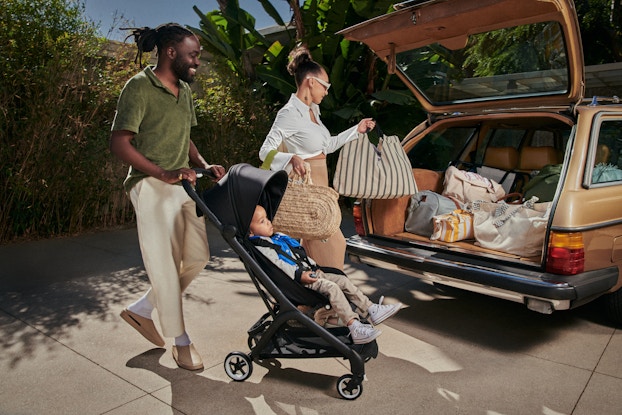 Two parents loading the trunk of their car while their child sits in a Bugaboo stroller.