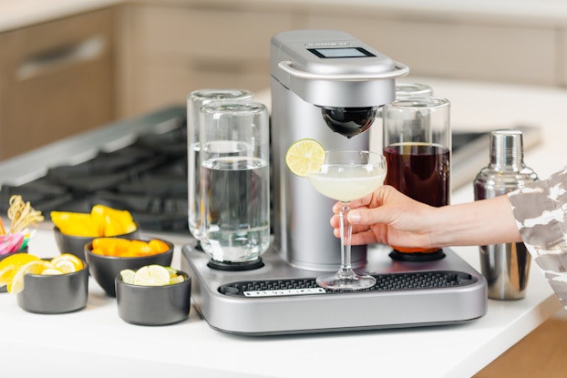 Person's hand holding a cocktail being created by the Bartesian cocktail machine.
