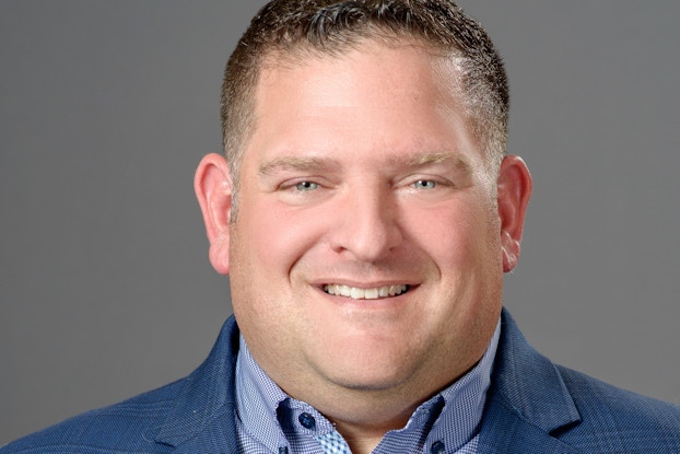 A headshot of Bill Catania, CEO of OneRail. Bill is a white man with dark blonde hair and light blue eyes. He's wearing a light blue button-up shirt and a navy blue blazer.
