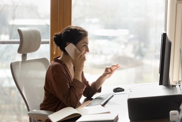 Confident woman in her home office looking at a computer screen and talking on the phone.