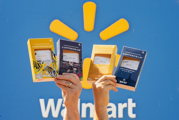  Two hands holding up Bean Box Coffeegrams in front of the Walmart logo.