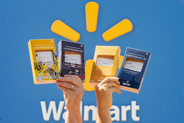 Two hands holding up Bean Box Coffeegrams in front of the Walmart logo.