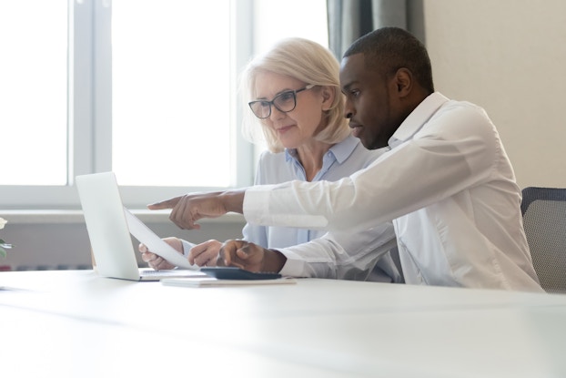 Employee pointing at laptop discussing information with colleague.
