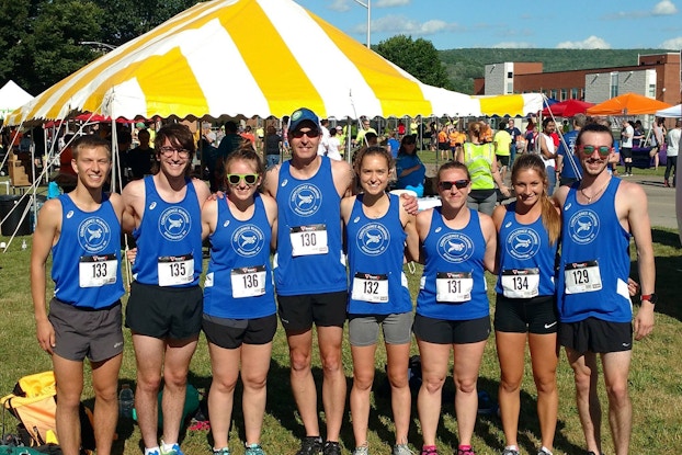 Running race participants pose outdoors with race bibs