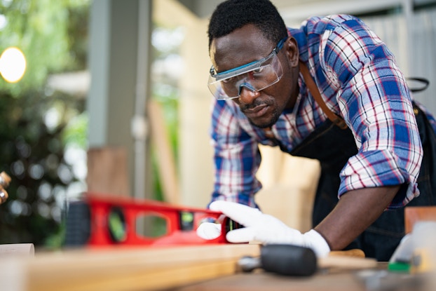  Close-up of a craftsman using a level to measure distance on wood plank.