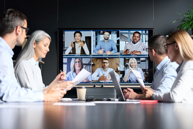 Meeting with some employees on videoconference and others in modern meeting room.