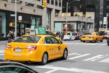  Yellow taxicab with a Curb advertising topper driving in the streets of New York City. 