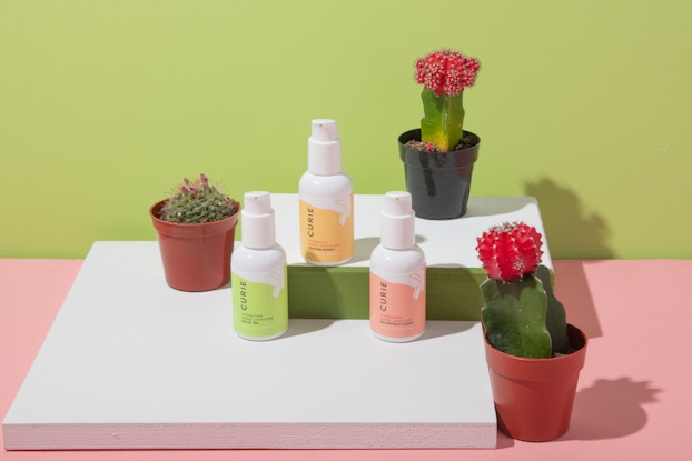  Product display of hand sanitizers by Curie on a countertop with potted succulent plants.