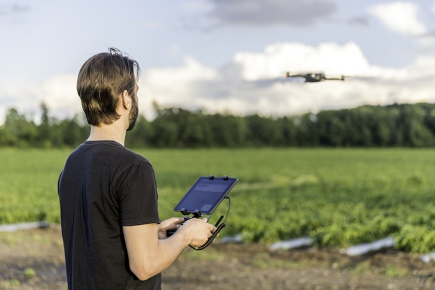  Farmer pilot using drone remote controller at sunset. The field is visible in the background