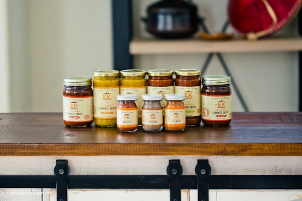 Multiple jars of products from Eleni's Kitchen are lined up on a countertop.