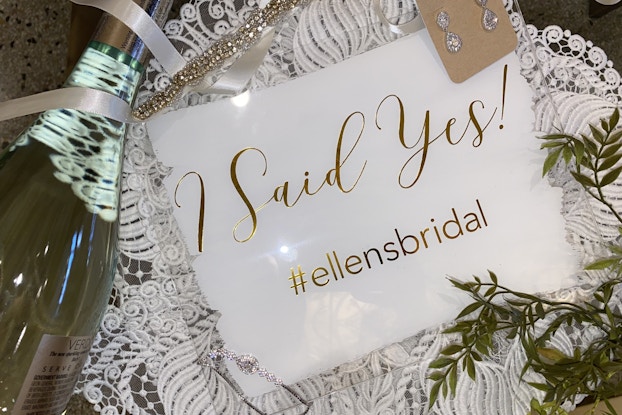 "I Said Yes!" sign with bridal earrings and a champagne bottle courtesy of Ellen's Bridal and Dress Shop.