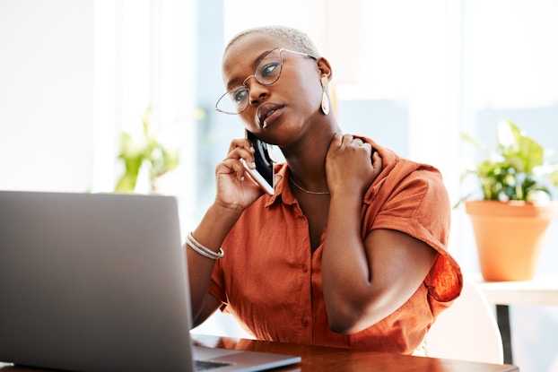 Concerned woman makes a phone call on her cell phone at her desk.