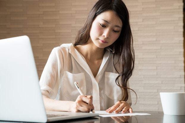  woman filling out paperwork next to computer