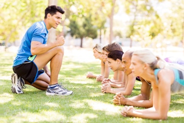  Fitness instructor motivating people doing exercise at park 