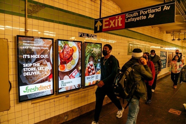 FreshDirect digital sign inside a New York City subway with people walking past it.