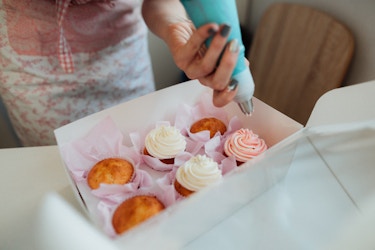 Person icing cupcakes that are packed in a to-go box.