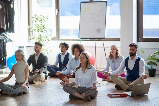  Group of employees in an office sitting on the floor participating in a yoga class.