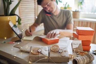 Man working on wrapping gifts at his desk while on the phone.