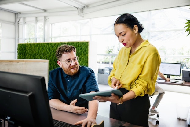  Manager showing employee something on a tablet inside an office.