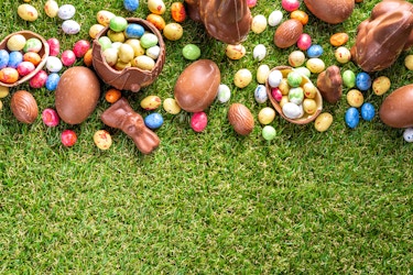  Chocolate Easter rabbits and foil-covered chocolate eggs spilled on a green lawn. 