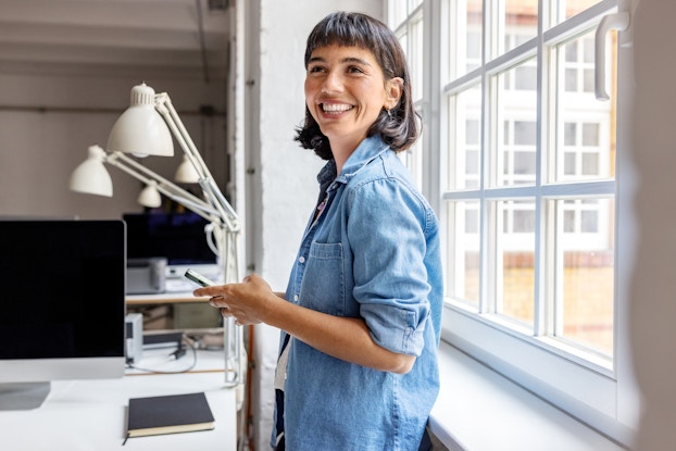 Smiling woman holding a phone inside of a bright office.