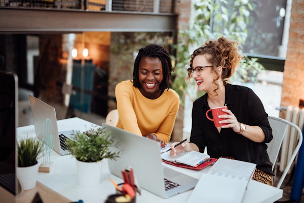  Two business women working at laptops at modern office