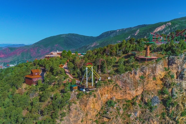  A longshot of Glenwood Caverns Adventure Park on top of a mountain in Glenwood Springs, Colorado. The park includes several wooden buildings, a roller coaster and two swinging structures.
