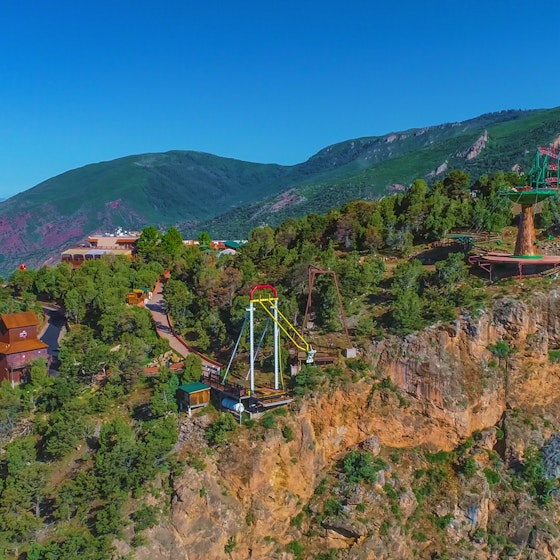  A longshot of Glenwood Caverns Adventure Park on top of a mountain in Glenwood Springs, Colorado. The park includes several wooden buildings, a roller coaster and two swinging structures. 