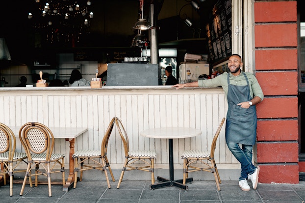 Successful entrepreneur smiles while he stands outside his cafe.