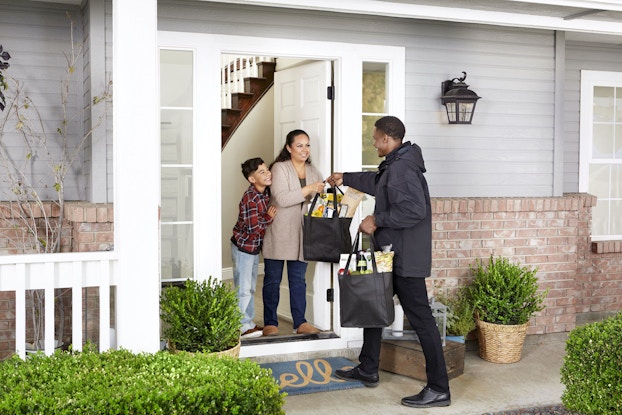 Albertsons employee delivering groceries to a customer and her child at their doorstep.