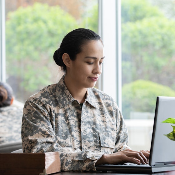 Woman wears military uniform and works on laptop in an office.
