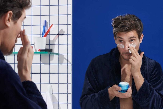 man using eye cream in bathroom mirror