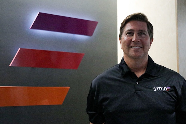 A shot of Jeff Stokes, president of STRIDE, standing next to the STRIDE logo (three parallel horizontal lines angled as if they're moving forward; the top line is purple, the middle red, and the bottom orange).