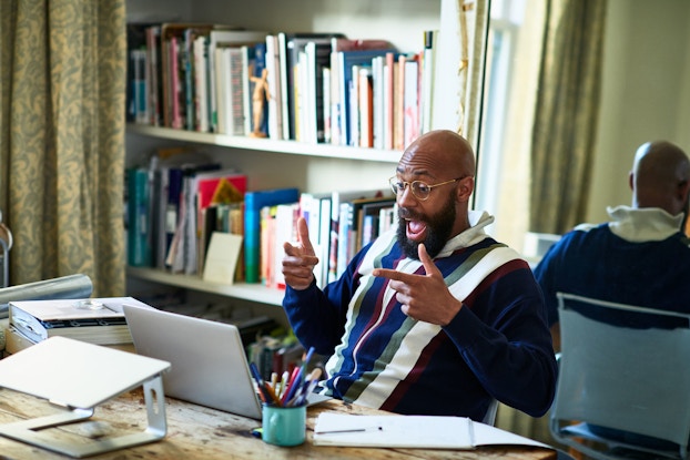  An entrepreneur who is seated at a desk before a laptop and is the middle of a video conference responds animatedly to something he has heard.