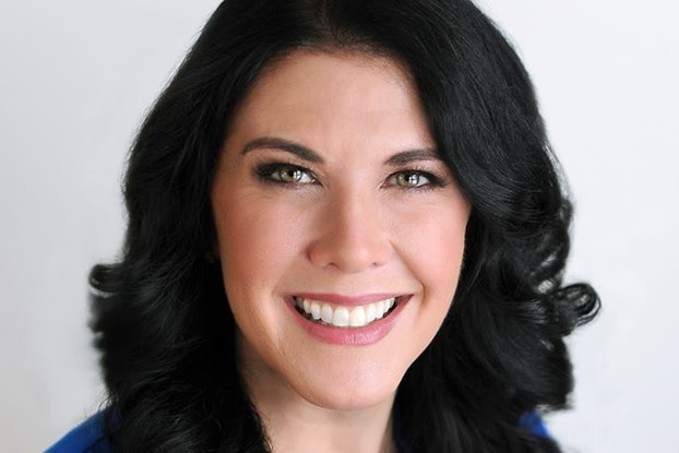 A headshot of Kelly Tope, Senior Director of Franchise Development at FullSpeed Automotive®. Tope is a white woman with long, curled black hair, and hazel eyes. She is smiling and wearing a cobalt blue blouse and a pendant necklace.