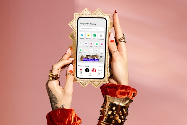 Person's hand wearing gold rings holding a phone in a spiky gold case with the Klarna app on the screen.