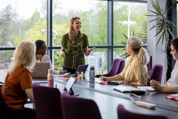 Smiling manager stands in a conference room and conducts a meeting with engaged employees.